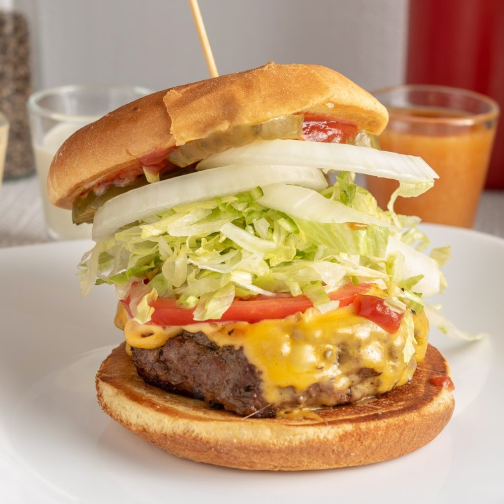 Classic cheeseburger with American cheese, lettuce, tomato, onion, and pickles on a bun.