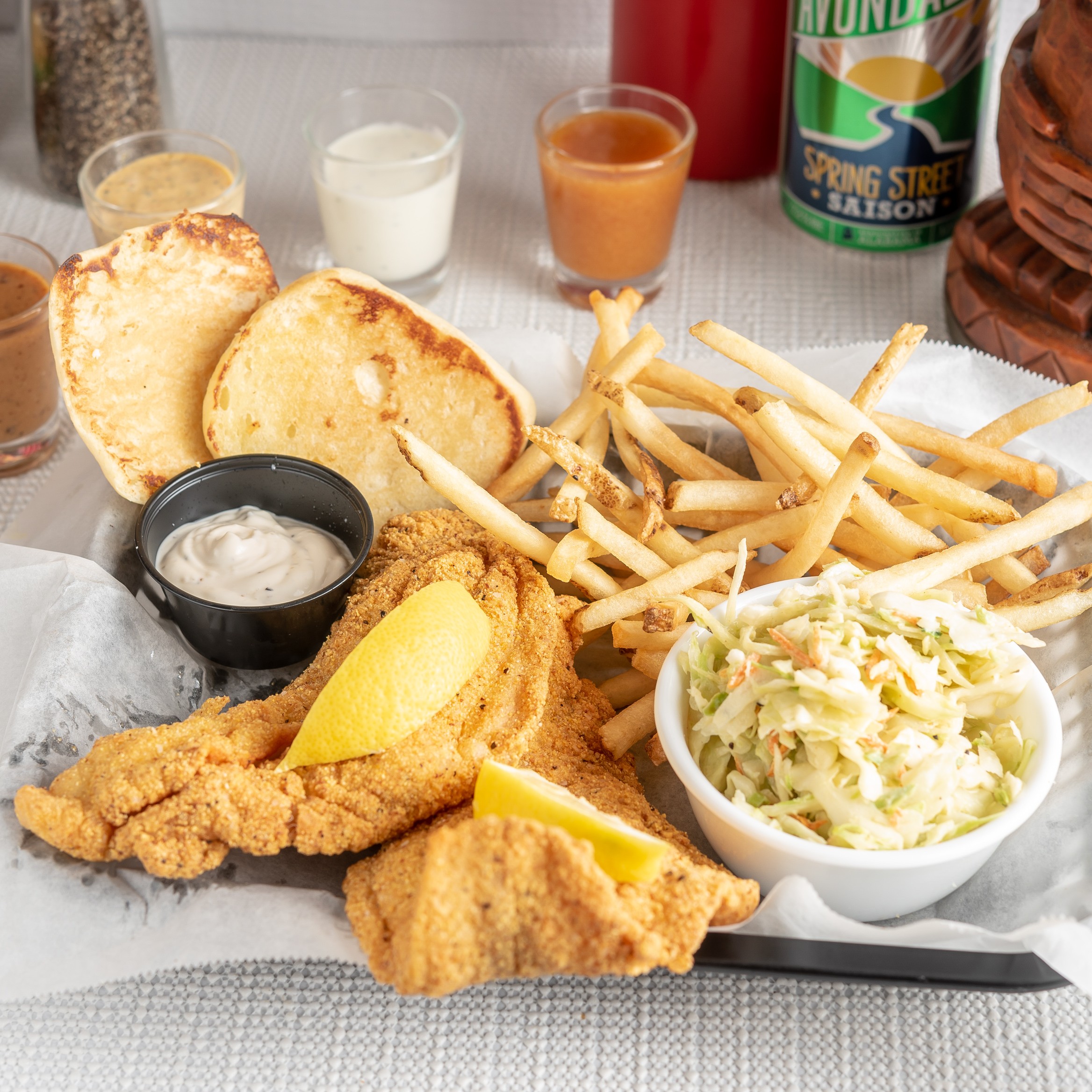 Fried catfish fillet with skinny fries, fruit, tartar sauce, and a roll.
