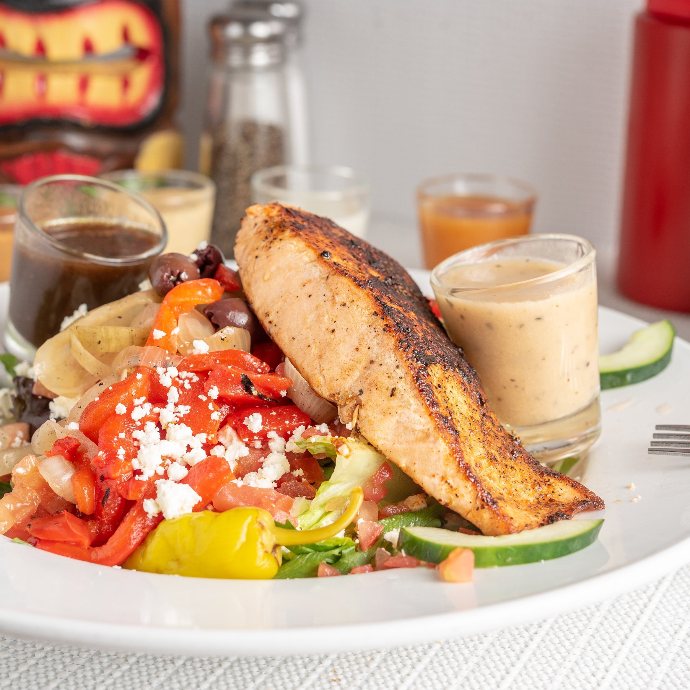 Grilled salmon fillet over mixed greens with tomatoes, cucumber, olives, peppers, and tzatziki.